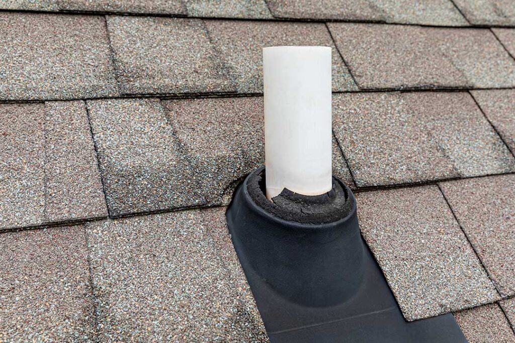 Person inspecting roof shingles and clearing leaves from a gutter beside a two-story home.