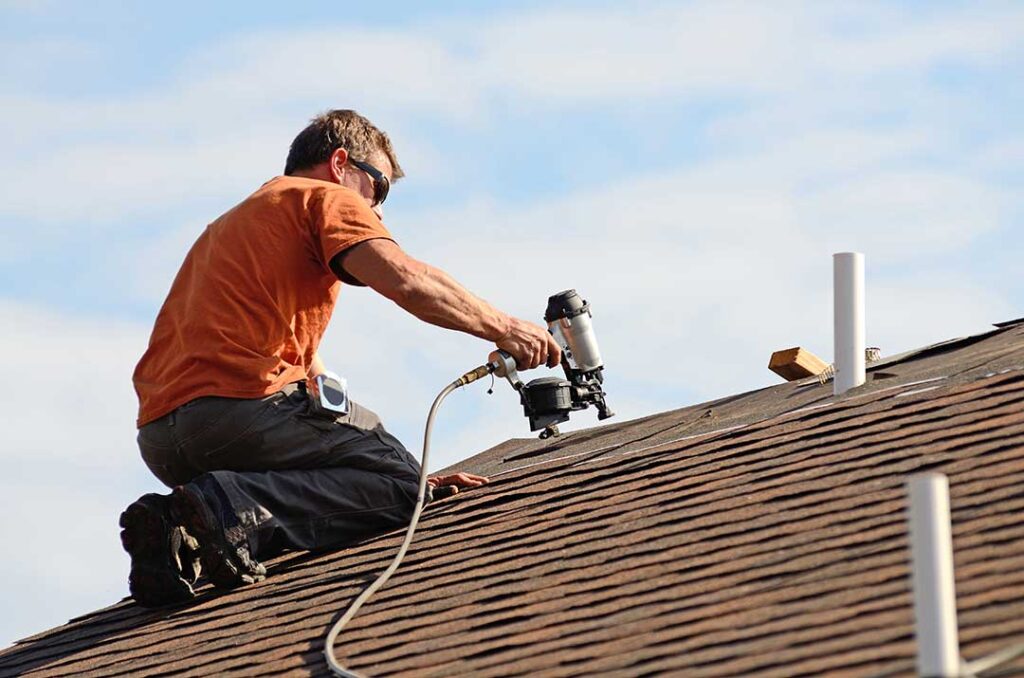 A homeowner examining attic insulation and roof vents beneath residential roof sheathing.