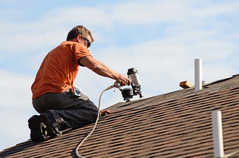A homeowner examining attic insulation and roof vents beneath residential roof sheathing.